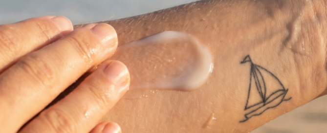 Persona che applica una crema solare su un tatuaggio al braccio in spiaggia, per proteggere la pelle dal sole e preservare il colore