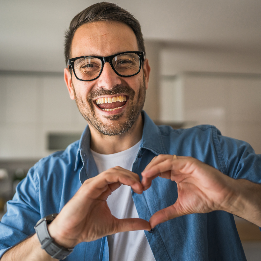 Uomo sorridente con gli occhiali forma un cuore con le mani, immagine dedicata alla prevenzione e alla salute cardiovascolare in occasione della Giornata Mondiale del Cuore.