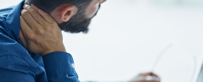 Uomo seduto davanti al computer che si tocca il collo per un fastidio cervicale, a rappresentare tensione e rigidità muscolare legate ai primi freddi.