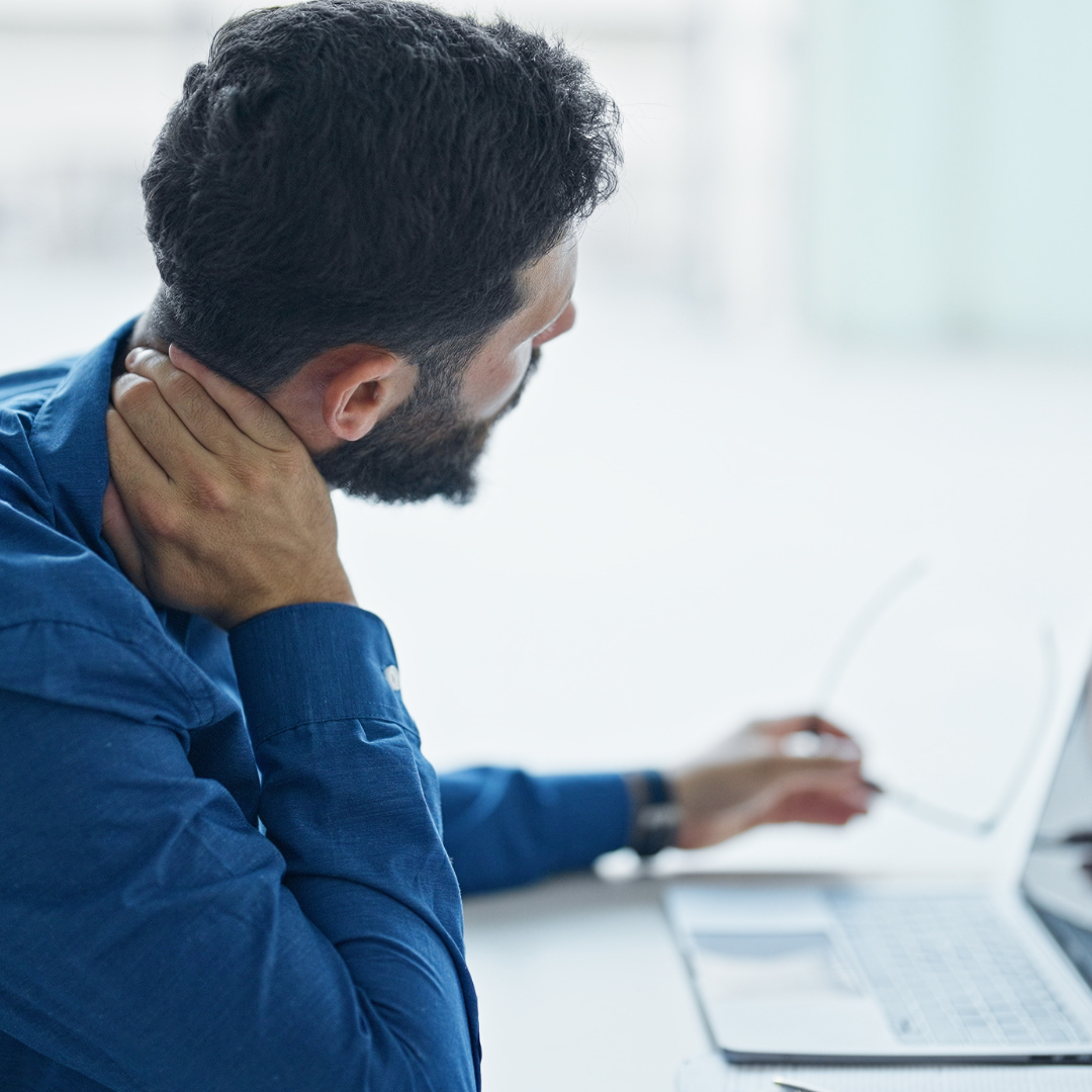 Uomo seduto davanti al computer che si tocca il collo per un fastidio cervicale, a rappresentare tensione e rigidità muscolare legate ai primi freddi.