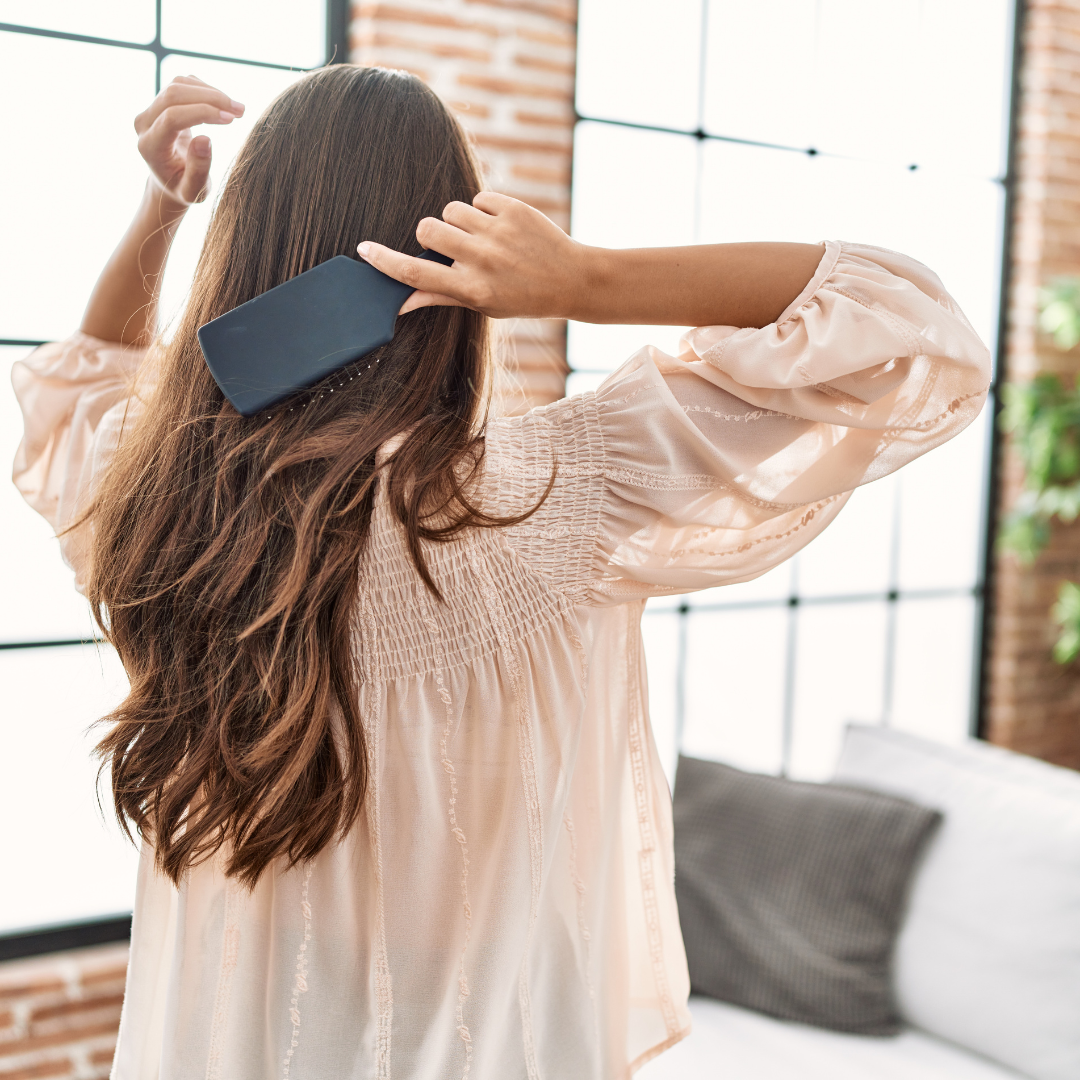 Donna vista di spalle mentre si spazzola i capelli lunghi, richiamando il naturale ricambio autunnale e l'importanza di prendersi cura del cuoio capelluto quando la caduta dei capelli appare più intensa o prolungata.